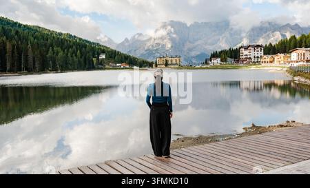 Una scena serena al Lago di Misurina, dove un viaggiatore ammira i riflessi mozzafiato delle maestose Dolomiti in Italia. Il paesaggio si dispiega wi Foto Stock