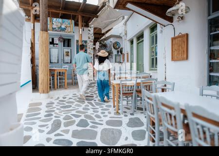 Una coppia cammina mano nella mano lungo le pittoresche strade acciottolate di Naxos, Grecia. Edifici vivaci e caffè accoglienti creano un'atmosfera romantica Foto Stock