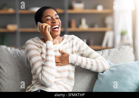 Piacevole chiamata. Allegra African American Woman Laughing mentre parla su Cellphone a casa, positivo Black Female godendo di conversazione sul telefono cellulare W Foto Stock
