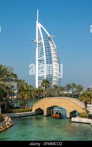 Tradizionale barca di legno abra che passa sotto un ponte ad arco in pietra con l'iconico Burj Al Arab a forma di vela sullo sfondo, Dubai, Emirati Arabi Uniti Foto Stock