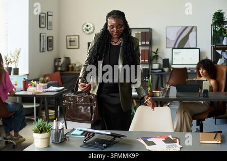 Donna d'affari nera che arriva sul luogo di lavoro in uno studio creativo d'ufficio Foto Stock