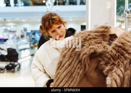 Ritratto di una giovane donna dai capelli rossi che prova un cappotto di pelliccia alla moda in negozio. sorriso positivo Foto Stock