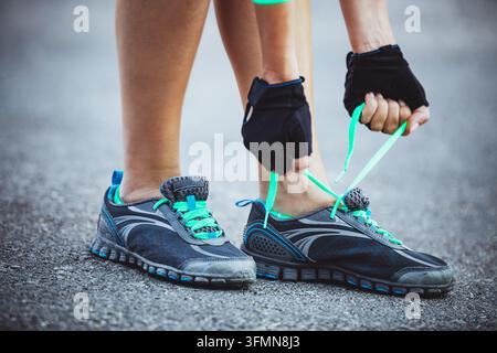 Donna che allaccia le scarpe da corsa prima di un allenamento all'aperto Foto Stock