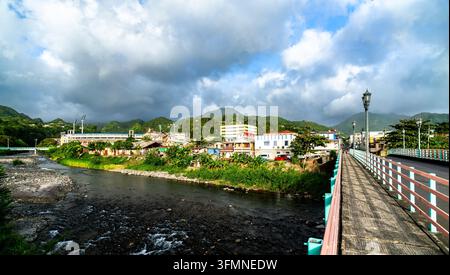 Bella vista del fiume Roseau che scorre attraverso Roseau, Dominica, da un ponte, con lo stadio sportivo Windsor Park e montagne lussureggianti sullo sfondo Foto Stock