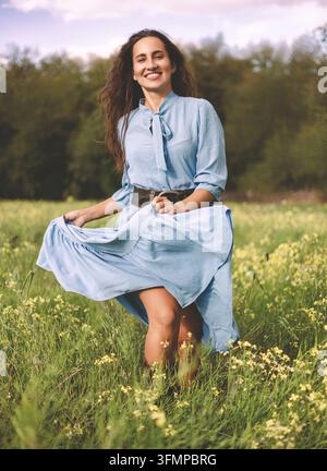 Giovane donna che corre attraverso un prato di fiori selvatici in un vestito blu Foto Stock