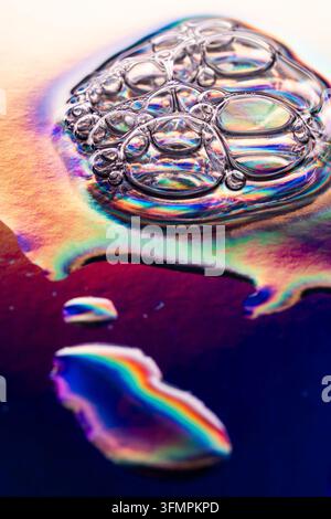 Vista macro di goccioline d'acqua limpide raggruppate su una superficie iridescente, che creano riflessi arcobaleno vividi, rifrazioni e motivi colorati astratti. Foto Stock