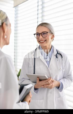 Dottoressa sorridente che consulta un collega in clinica Foto Stock