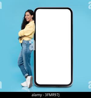 Giovane donna sorridente con lunghi capelli appoggiata su uno schermo di smartphone vuoto, spazio di copia Foto Stock