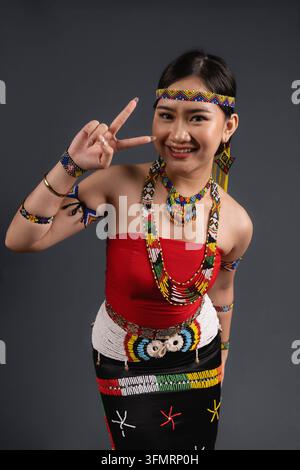Giovane malese sorridente in abito tradizionale Simba della tribù Murut Tahol di Sabah, Malesia, che mostra un segno di pace. Foto Stock