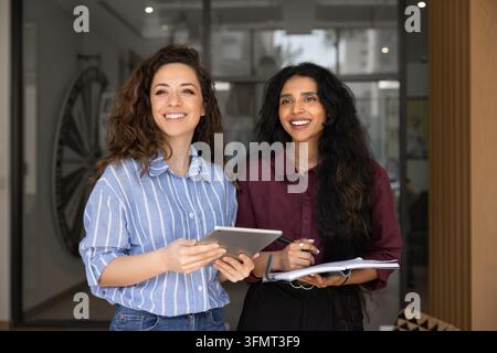 Colleghe donne multi etniche in piedi insieme con tablet digitale e documenti Foto Stock