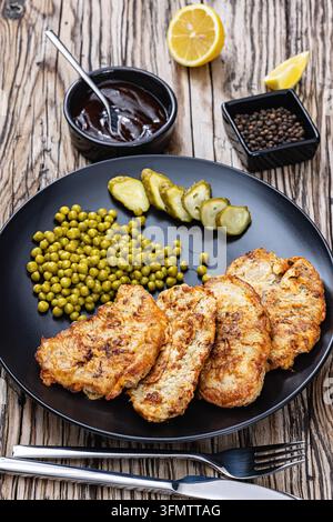 Veprovy rizek v testicku cucina ceca cotoletta di maiale fritta in pastella all'uovo servita con piselli verdi, sottaceti su un piatto, accompagnata da una salsa dunkle e le Foto Stock