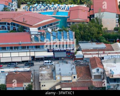 Laganas, Grecia, 1 settembre 2026: veduta aerea delle attività resort tra cui Sugar e Sirocco con appartamenti vicini, auto parcheggiate, tetti, satellite Foto Stock