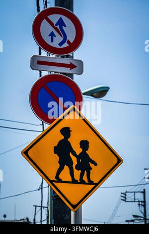 Un cartello giapponese a forma di rombo giallo per l'attraversamento scolastico, che mostra silhouette nere di un adulto e un bambino che si tengono per mano, è ben visibile bel Foto Stock