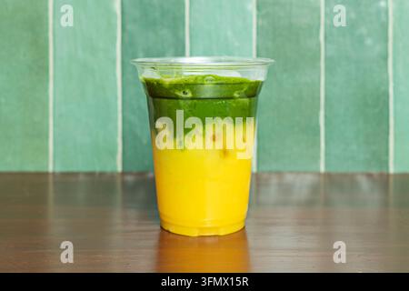 Bevanda a strati di arancia e matcha in una tazza trasparente su uno sfondo di legno verde Foto Stock