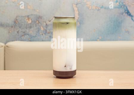 Latte al matcha a strati in una lattina alta su un tavolo di legno contro un muro blu sbiadito Foto Stock