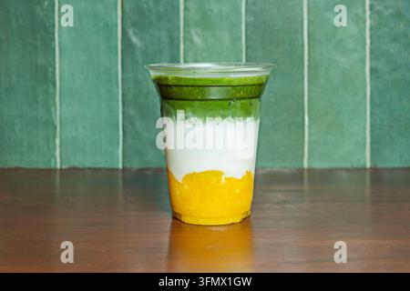 Bevanda a strati di mango e matcha in un bicchiere di plastica appoggiato su un tavolo di legno scuro Foto Stock