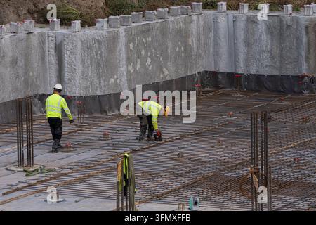 Operai edili che installano rinforzi in acciaio all'interno di pareti di fondazione in cemento, concetto di cantiere per infrastrutture Foto Stock