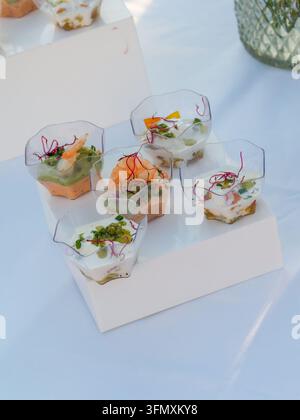 Varietà di antipasti di frutti di mare gourmet serviti in piccole ciotole trasparenti su un tavolo bianco durante un evento all'aperto. Foto Stock