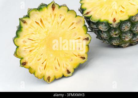 Ananas tagliato a metà che mostra la polpa gialla fibrosa e la buccia verde accanto a un ananas intero su uno sfondo bianco da studio Foto Stock