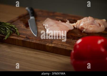 Filetti di pollo crudi su tagliere con coltello Foto Stock