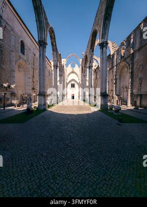Interno illuminato dal sole delle rovine del Convento do Carmo a Lisboa, Portogallo, con archi gotici svettanti, mura di pietra storiche e un cortile lastricato sottostante Foto Stock