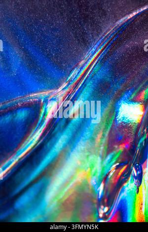 Vista macro astratta di materiale olografico iridescente con riflessi arcobaleno vividi, pieghe fluide e colori blu, verdi, rosa e viola luminosi Foto Stock