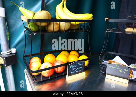Mele fresche, arance, banane, pere e kiwi disposti in cesti su un piccolo banco di alimentari. Esposizione di frutta colorata con prezzi scritti a mano, illustr Foto Stock