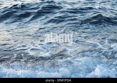 Prima vista di onde oceaniche increspate e acqua di mare schiumosa, che creano una texture superficiale blu naturale con movimento delicato, bolle e spruzzi bianchi Foto Stock