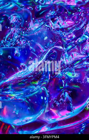 Primo piano astratto di forme liquide iridescenti e lucide con bolle, che riflettono una vivida luce blu neon, ciano, viola e magenta in un tè fluido futuristico Foto Stock