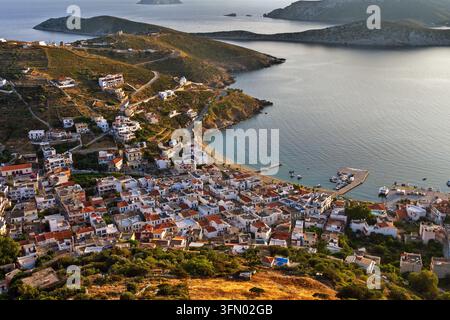 Vista aerea di Fournoi, Grecia, Europa, alla luce dorata, che mostra il villaggio compatto sul lungomare, il piccolo porto, le barche da pesca e le strade tortuose Foto Stock