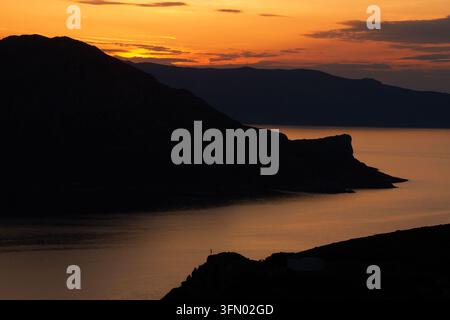 Tramonto infuocato sul Mar Egeo a Fournoi, Grecia, che siluetta creste frastagliate delle isole e promontori rocciosi sopra acque calme luminose. Foto Stock