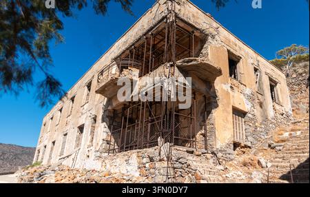 La rudere dell’ospedale di cemento abbandonato sull’isola di Spinalonga, rinforzata con pilastri di sostegno in acciaio provvisori a più piani per prevenire il crollo a Creta, Gre Foto Stock