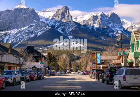 Canmore, Alberta, Canada - 02 12 2025: Vista di una luminosa giornata invernale soleggiata che guarda giù per la strada del centro città in una città di montagna fiancheggiata da edifici in stile alpino, Foto Stock