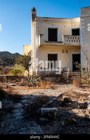 Facciata di edificio abbandonato con finestre rotte e un balcone in cemento danneggiato che presenta un aspetto inquietante e spettrale a Creta, Grecia Foto Stock