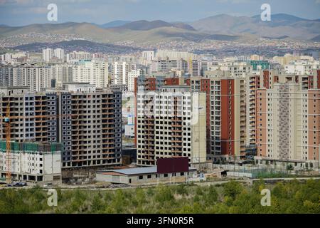 Una vista aerea grandangolare di Ulaanbaatar mostra diversi grattacieli residenziali in cemento grigio incompiuti in primo piano, con edifici chiari completati Foto Stock