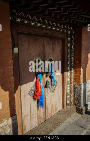 Una porta di legno consumata, probabilmente su un tempio o un monastero, presenta due batacchie in ottone ornate a forma di teste di drago o di leone, ciascuna adornata con Foto Stock