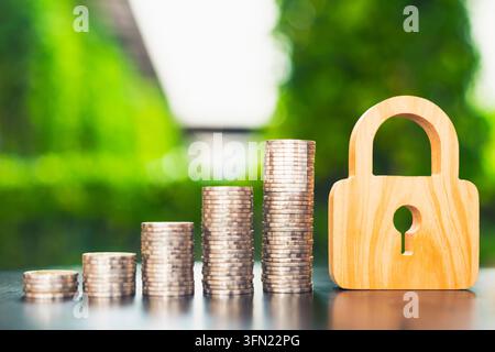 Concetto di sicurezza finanziaria e protezione del denaro, lucchetto di legno accanto a pile crescenti di monete d'argento sul tavolo, che rappresenta la sicurezza del capitale Foto Stock