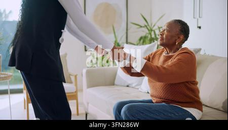 Aiutare, vecchia donna e tenersi per mano con l'infermiera nella casa di cura, connessione o assistenza nel salone. Assistenza sanitaria, badante e persona anziana nera nel Foto Stock