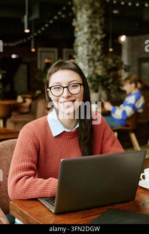 Ritratto di una donna sorridente che usa un laptop in un caffè per il lavoro da remoto Foto Stock