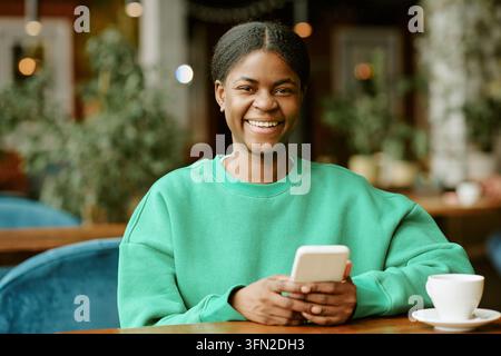 Ritratto di una donna nera felice che tiene uno smartphone in un caffè Foto Stock