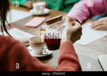 Donna che versa tè caldo alle erbe in una tazza con amici in un caffè Foto Stock