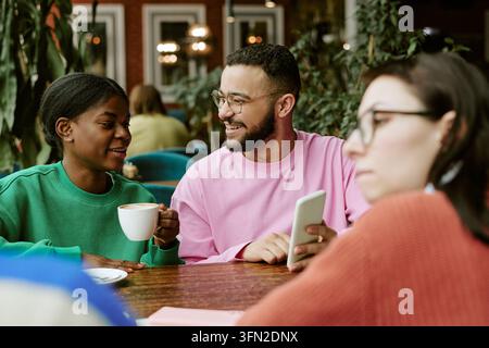 Gruppo diversificato di amici che parlano e guardano uno smartphone in un caffè Foto Stock