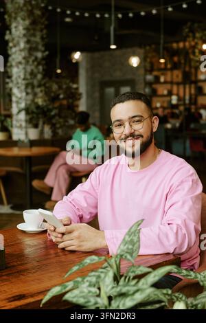 Ritratto di un uomo biracial sorridente che tiene uno smartphone in un caffè Foto Stock
