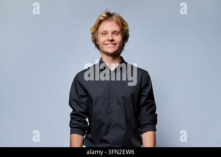 Giovane uomo sorridente con capelli biondi che guarda la fotocamera su uno sfondo grigio chiaro Foto Stock