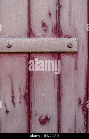 Antica porta di legno viola con vernice scrostata, superficie consumata, dettaglio serratura in metallo, viti, sfondo texture vintage rustico Foto Stock