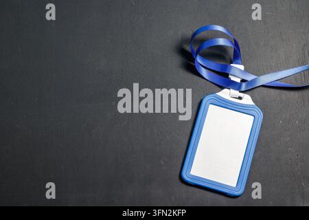 Un portabadge in plastica blu vuoto con un cordino a nastro appoggiato su uno sfondo scuro testurizzato, ideale per conferenze aziendali o mockup aziendali. Foto di alta qualità Foto Stock