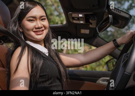 Giovane donna asiatica sorridente che tiene il volante mentre guida la sua auto moderna. Foto Stock