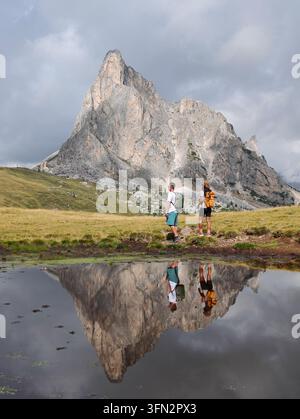 Avventurieri attraversano il maestoso Passo Giau nelle Dolomiti, Italia, con riflessi montani suggestivi in uno stagno tranquillo. Foto Stock