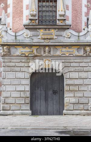 Vista dell'ingresso in pietra ornato e della porta in legno del grande arsenale storico con intagli dettagliati e facciata in mattoni a Danzica, Pomerania Foto Stock