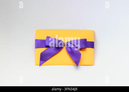 Busta gialla legata con un fiocco di raso viola, isolata su sfondo bianco. Concetto di regalo, invito e celebrazione. Foto Stock